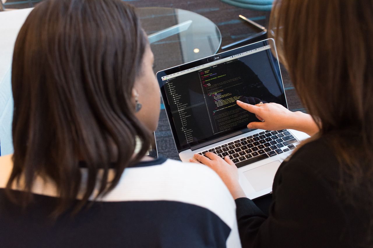 Two learners reviewing programming code together on a laptop