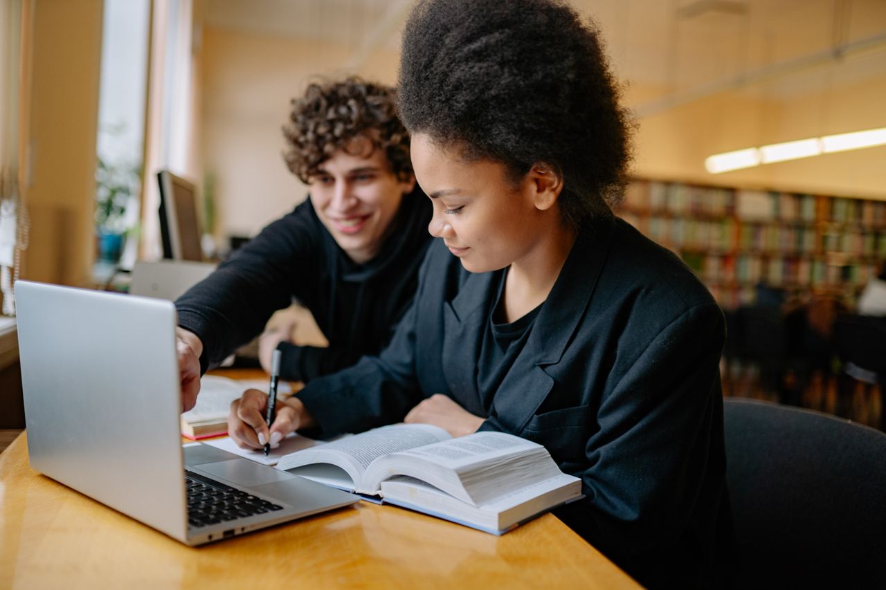 Two students reviewing notes beside a laptop in a library