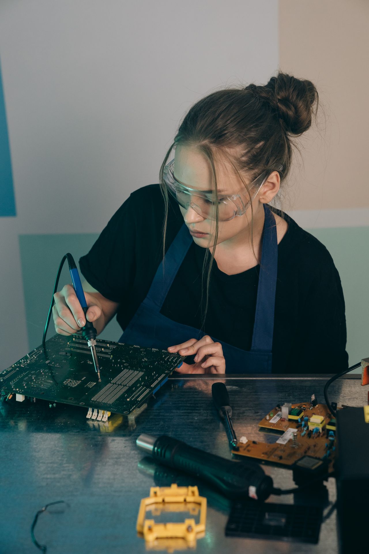 An engineer wearing safety goggles and soldering a circuit board