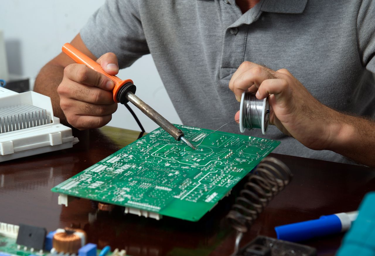 Hands carrying out precise soldering work on a circuit board