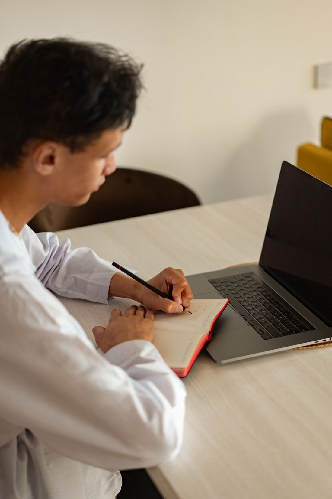 A learner taking notes beside a laptop during an online lesson